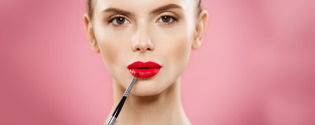 Schoonheidsconcept Vrouw die rode lippenstift met roze studioachtergrond toepast Mooi meisje maakt make-up