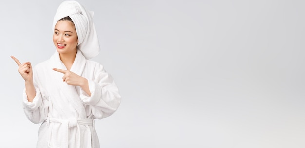 Schoonheidsportret van een jonge vrouw die met de vinger wijst naar lege kopieerruimte Aziatische schoonheid in badjas
