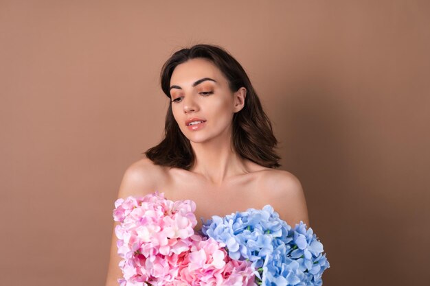 Schoonheidsportret van een topless vrouw met een perfecte huid en natuurlijke make-up op een beige achtergrond met een boeket van kleurrijke bloemen