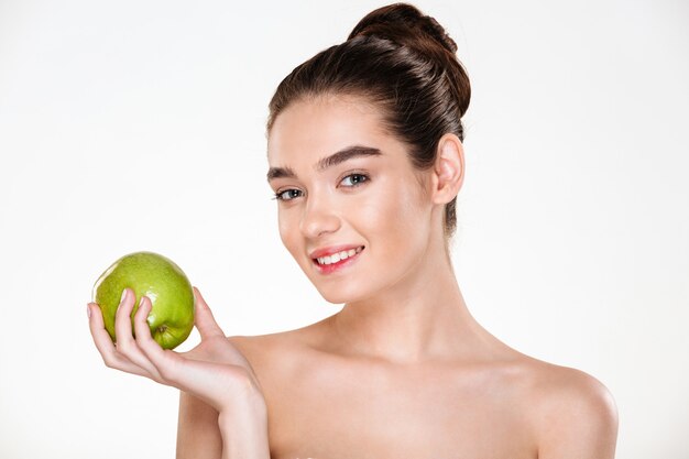 Schoonheidsportret van mooie glimlachende vrouw met zachte huid die groene appel bij haar palm en het kijken houden