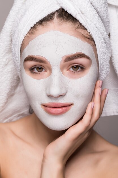 Schoonheidsportret van vrouw in handdoek op hoofd met wit voedend masker of room op gezicht, witte geïsoleerde muur. Huidverzorging reinigende eco organische cosmetische spa ontspannen concept