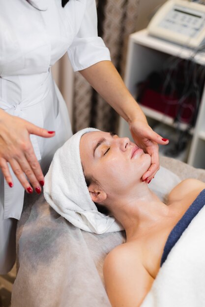 Schoonheidsspecialiste in een spa-schoonheidssalon past crème toe op het gezicht van een klant, een meisje ligt op een cosmetologie-tafel