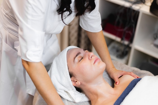 Schoonheidsspecialiste in een spa-schoonheidssalon past crème toe op het gezicht van een klant, een meisje ligt op een cosmetologie-tafel