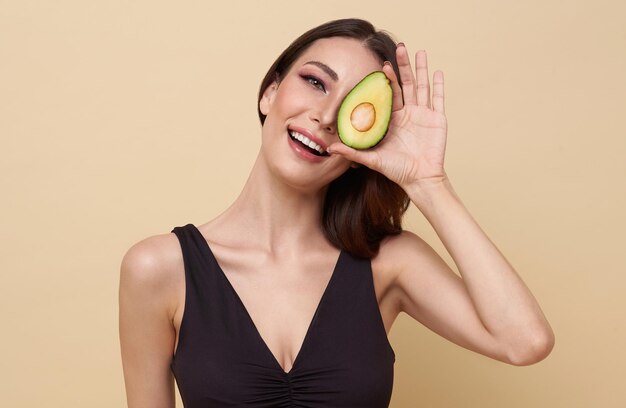 Schoonheidsvrouw houdt een halve avocado voor haar gezicht