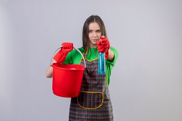 schoonmaak jonge vrouw dragen uniform in rode handschoenen houden emmer stak schoonmaak spray op geïsoleerde witte muur