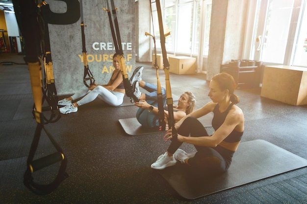 Schorsing die drie jonge atletische vrouwen traint die op yogamatten in de sportschool zitten en oefenen met