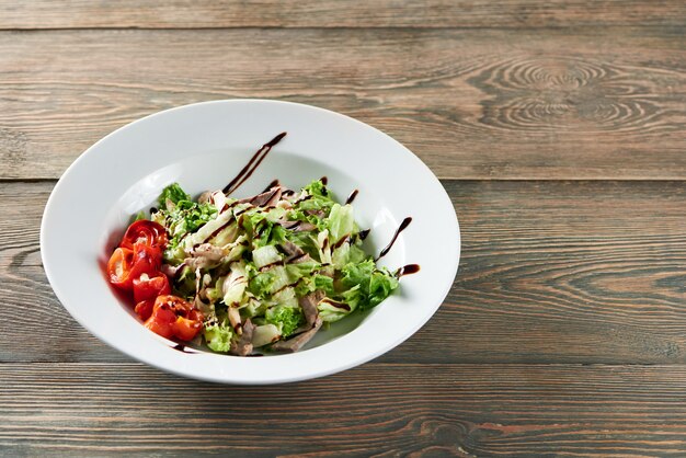 Schot van heerlijke salade met kip versierd met tomaten en saus op houten tafel copyspace delicatesse smakelijke eetlust honger menu restaurant café lunch maaltijd diner concept.