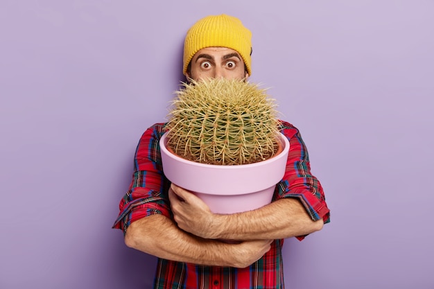 Gratis foto schot van verrast tuinman poseren met een grote ingemaakte cactus
