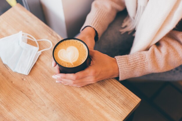 Schot van vrouw handen houden kopje warme koffie met hart ontwerp gemaakt van schuim.