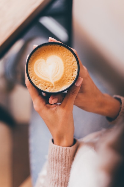 Schot van vrouw handen houden kopje warme koffie met hart ontwerp gemaakt van schuim.