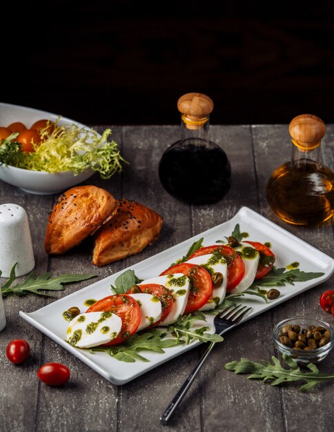 Schotel van carpese salade gegarneerd met basilicumbladeren en olijven