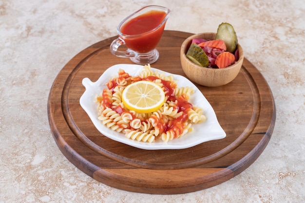 Schotel van gekookte pasta, ketchup en een kom gemengde augurken op marmeren oppervlak