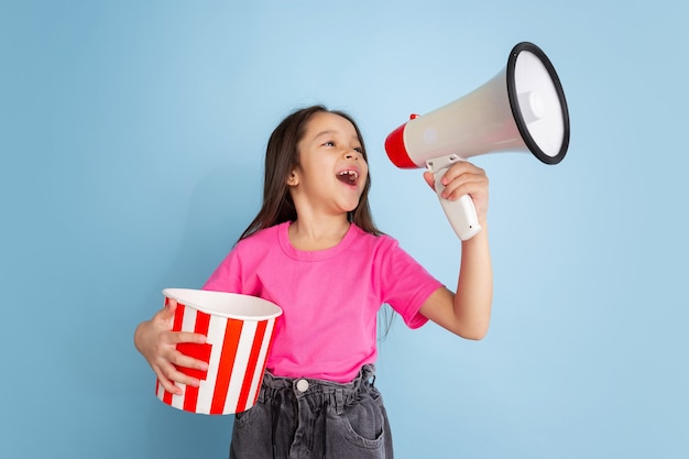 Schreeuwen met popcorn. Het portret van het Kaukasische meisje op blauwe muur. Mooi vrouwelijk model in roze overhemd. Concept van menselijke emoties, gezichtsuitdrukking, jeugd, jeugd.