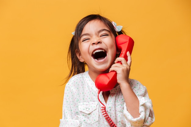 Schreeuwend opgewonden meisje kind praten door rode retro telefoon.