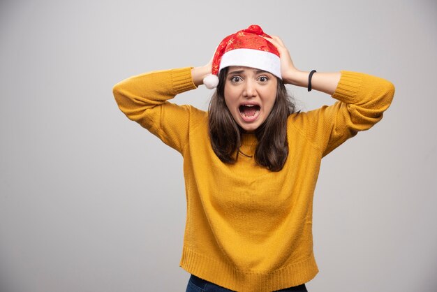 Schreeuwende vrouw in de rode hoed van de Kerstman die over een witte muur stelt.