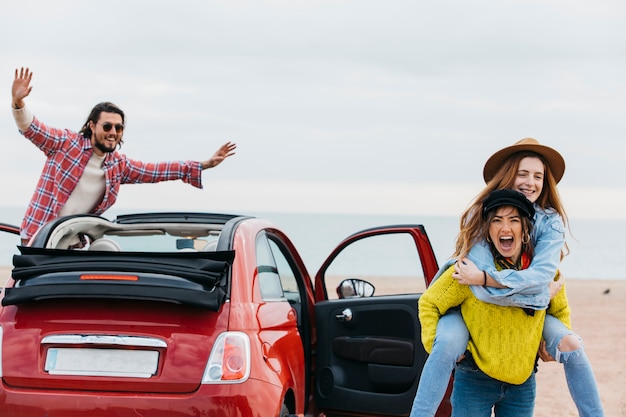 Gratis foto schreeuwende vrouwenholding op achter gelukkige dame dichtbij de mens die uit van auto leunt