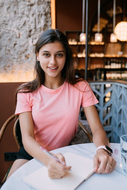 Schrijven van zuivel in nota in coffeeshop, concept als herinnering aan het leven. Vrouw in coffeeshop. Glimlachende vrouw die notities Kladblok maakt.