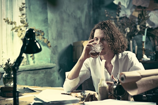 Schrijver aan het werk. Knappe jonge schrijver zitten aan de tafel en iets te schrijven in zijn schetsblok