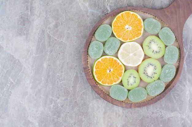 Segmenten van citrusvruchten, kiwi en snoepjes op een houten bord.