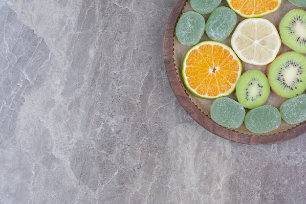 Segmenten van citrusvruchten, kiwi en snoepjes op een houten bord.