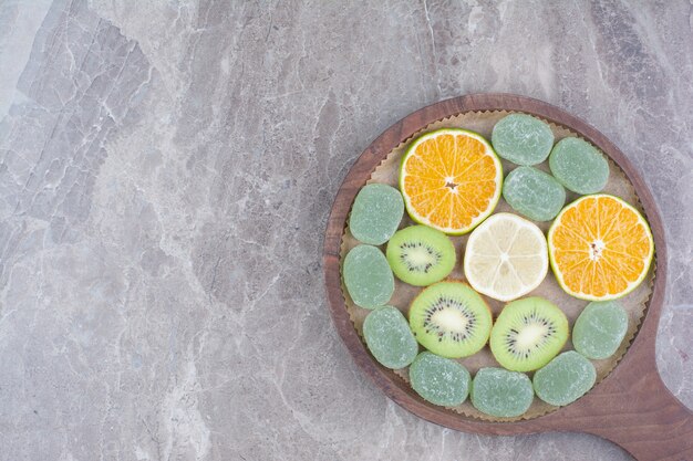 Segmenten van citrusvruchten, kiwi en snoepjes op een houten bord.