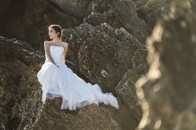 Selectieve aandacht shot van een brunette vrouw in een witte jurk die zich voordeed op de rotsen