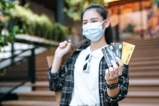 Selectieve focus creditcard in de hand van een jonge Aziatische vrouw met een beschermingsmasker dat op de trappen van het winkelcentrum staat