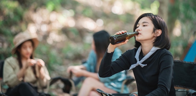 Selectieve focus jonge Aziatische mooie vrouw en haar vriendin zitten aan de voorkant van de tent gebruiken mobiele telefoon om foto te maken tijdens het kamperen in het bos met geluk samen