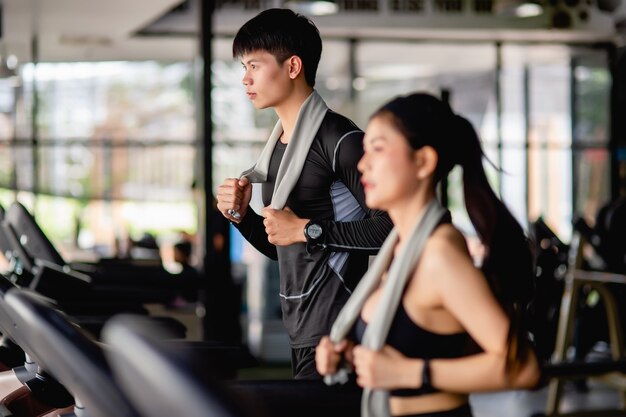 Selectieve focus jonge man, wazige jonge sexy vrouw op de voorgrond die sportkleding en smartwatch draagt, ze lopen op de loopband om te trainen in de moderne sportschool,