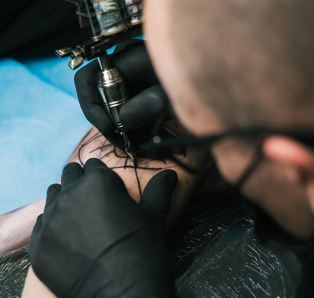 Selectieve focus shot van een tatoeëerder met zwarte handschoenen die een tatoeage op de arm van een man maken