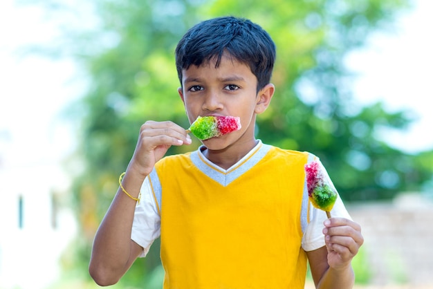 Selectieve focus van een kleine Indiase jongen die gearomatiseerde kleurrijke ijsgola eet