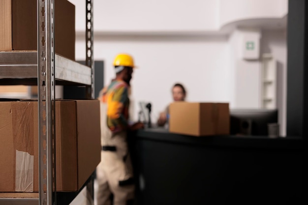 Selectieve focus van metalen planken in opslagruimte, vol met kartonnen dozen klaar voor levering. Op de achtergrond een divers team dat werkt aan bestellingen van klanten, pakketten klaarmaakt tijdens goedereninventarisatie