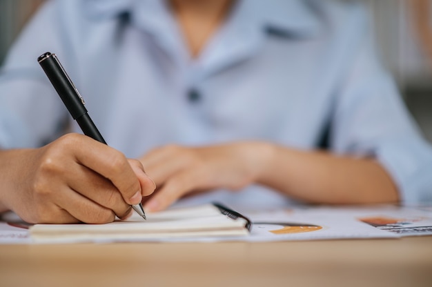 Selectieve focushand van aziatische jonge vrouw in brillen gebruiken pen werken met papieren op kantoor aan huis, tijdens quarantaine covid-19 zelfisolatie thuis, werk vanuit huis concept