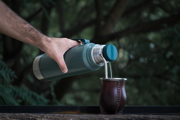 Selectieve focusopname van een hand die water uit een thermoskan in een kopje giet