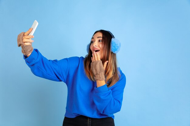 Selfie. Blanke vrouw portret op blauwe ruimte. Mooi vrouwelijk model in warme kleren