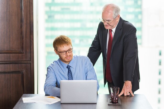 Senior business man kijkt naar het werk van een andere jongere werknemer