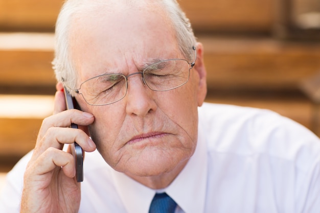 Senior business man met gesloten ogen tijdens het praten aan de telefoon