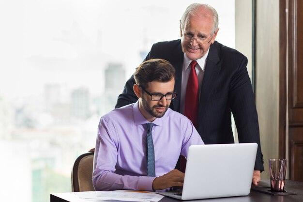 Senior business man op zoek naar hoe een andere jongere man werken