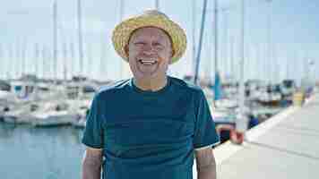 Gratis foto senior grijsharige man toerist met zomerhoed glimlachend in de haven