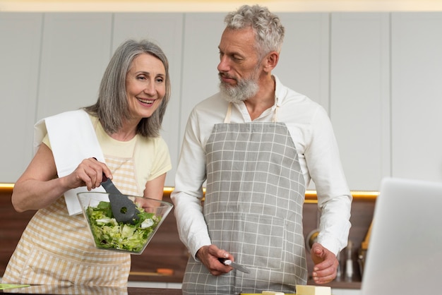 Gratis foto senior koppel thuis in de keuken kooklessen nemen op laptop