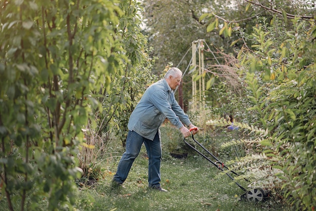 Senior maait het gras in de tuin met een grasmaaier