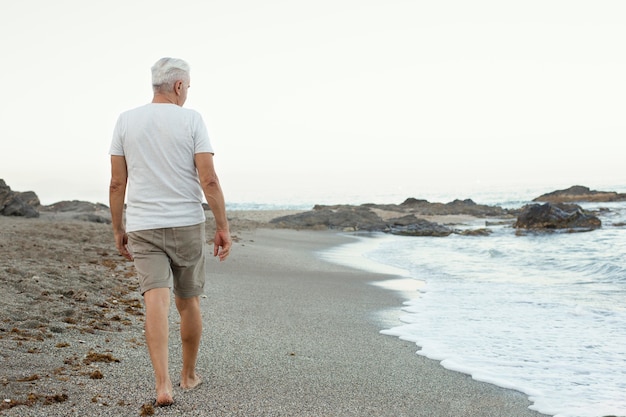 Senior man die alleen op het strand loopt