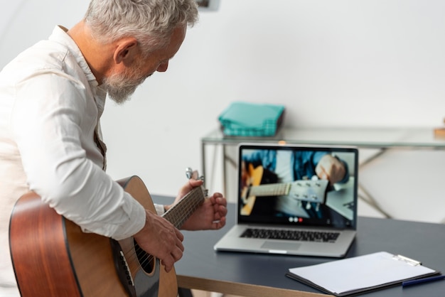 Senior man die thuis gitaarlessen studeert op laptop