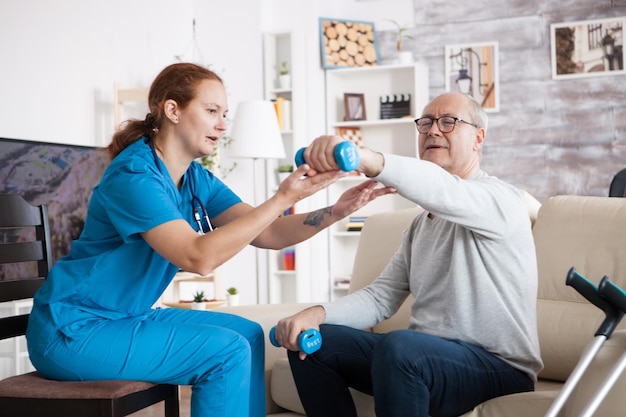 Senior man in verpleeghuis met fysiotherapie met hulp van verpleegkundige met halters.