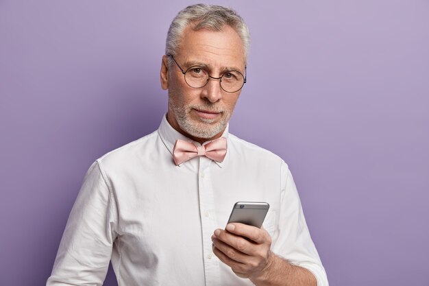 Senior man in wit overhemd en roze bowtie met telefoon