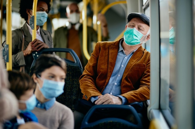 Senior man met beschermend gezichtsmasker aan het dutten tijdens het woon-werkverkeer met de bus