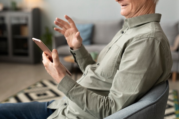 Senior man met een video-oproep met behulp van tablet zittend op een stoel in de woonkamer