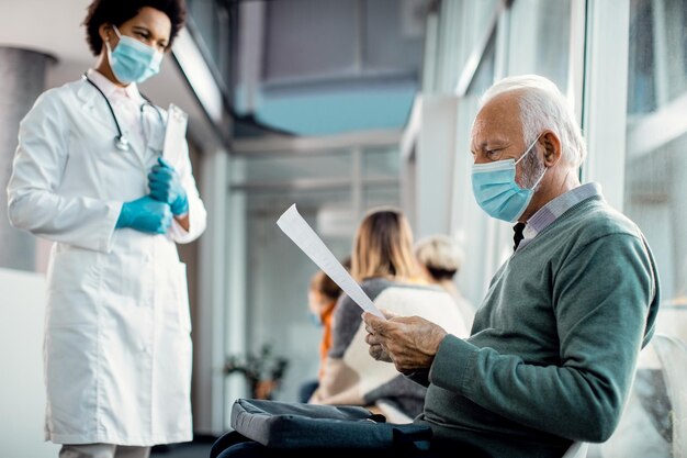 Senior man met gezichtsmasker die zijn medisch rapport leest in het ziekenhuis