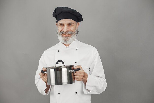 Senior man met metalen pan. Chef-kok in een zwarte hoed. Professionele benadering van zaken.