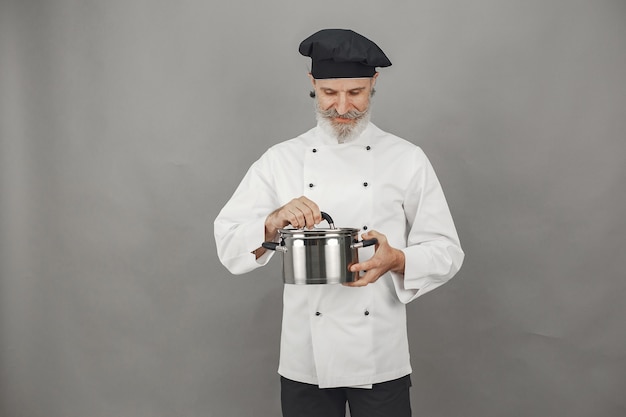 Senior man met metalen pan. Chef-kok in een zwarte hoed.